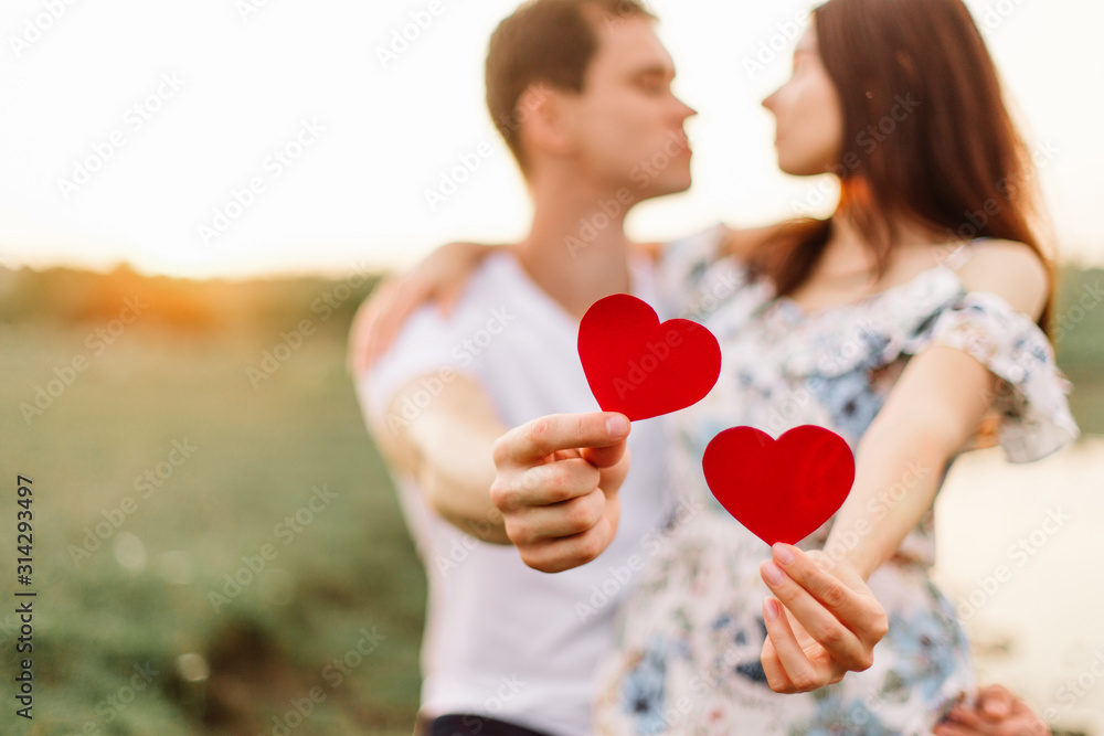 Young loving couple hugging near lake with red paper heart in hand. Young loving couple hugging near lake with red paper heart in hand.