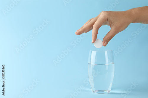 Woman putting tablet into glass of water on light blue background, space for text