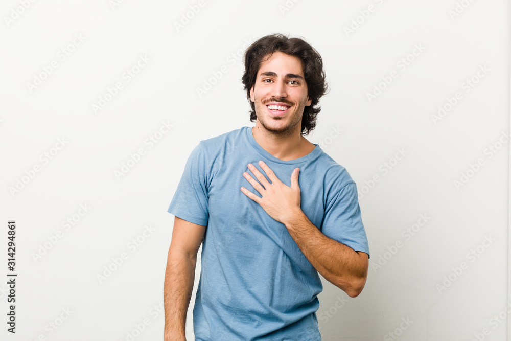 Young handsome man against a white background laughs out loudly keeping hand on chest. Young handsome man against a white background laughs out loudly keeping hand on chest.