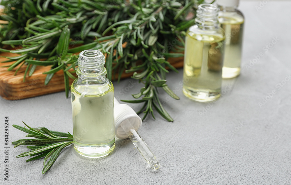 Fresh rosemary and bottle of essential oil on light grey table. Space or text Fresh rosemary and bottle of essential oil on light grey table. Space or text