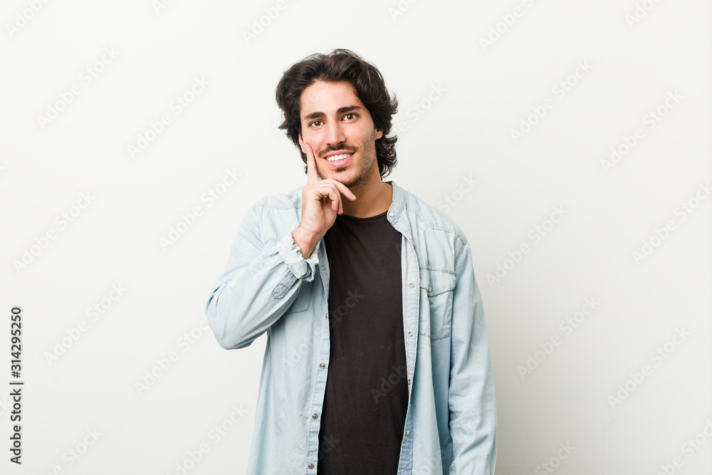 Young handsome man against a white background smiling happy and confident, touching chin with hand. Young handsome man against a white background smiling happy and confident, touching chin with hand.