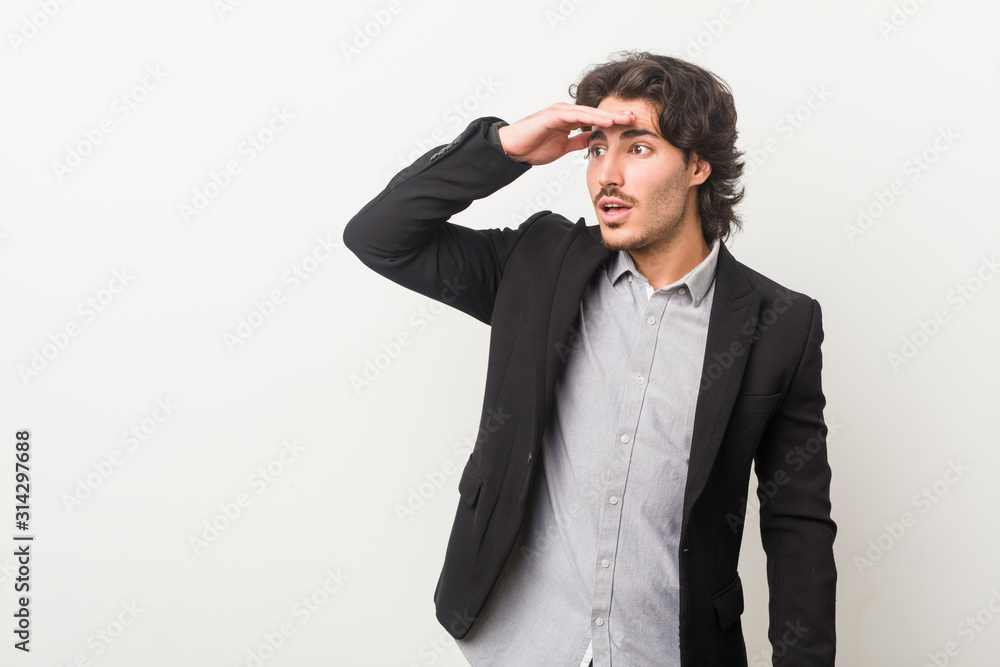 Young business man against a white background looking far away keeping hand on forehead. Young business man against a white background looking far away keeping hand on forehead.