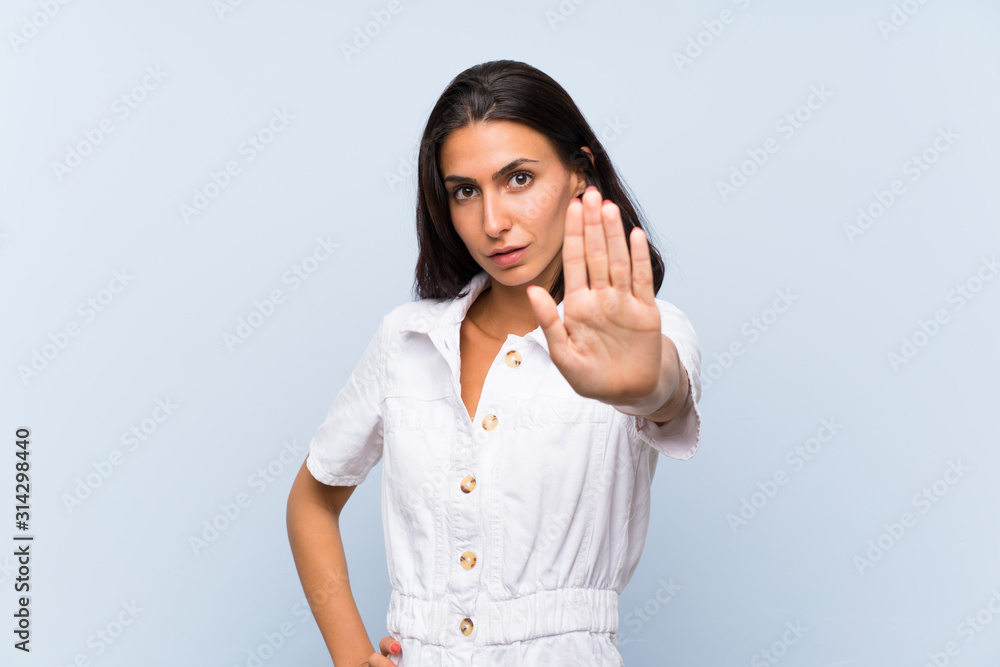 Young woman over isolated blue background making stop gesture with her hand Young woman over isolated blue background making stop gesture with her hand