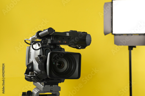Professional video camera and lighting equipment on yellow background