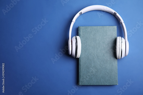 Book and modern headphones on blue background, top view. Space for text