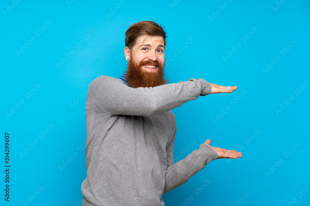 Redhead man with long beard over isolated blue background holding copyspace to insert an ad Redhead man with long beard over isolated blue background holding copyspace to insert an ad