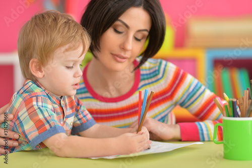 young mother and her little son drawing together with pencils