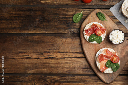 Puffed rice cakes with prosciutto, tomato and basil on wooden table, flat lay. Space for text