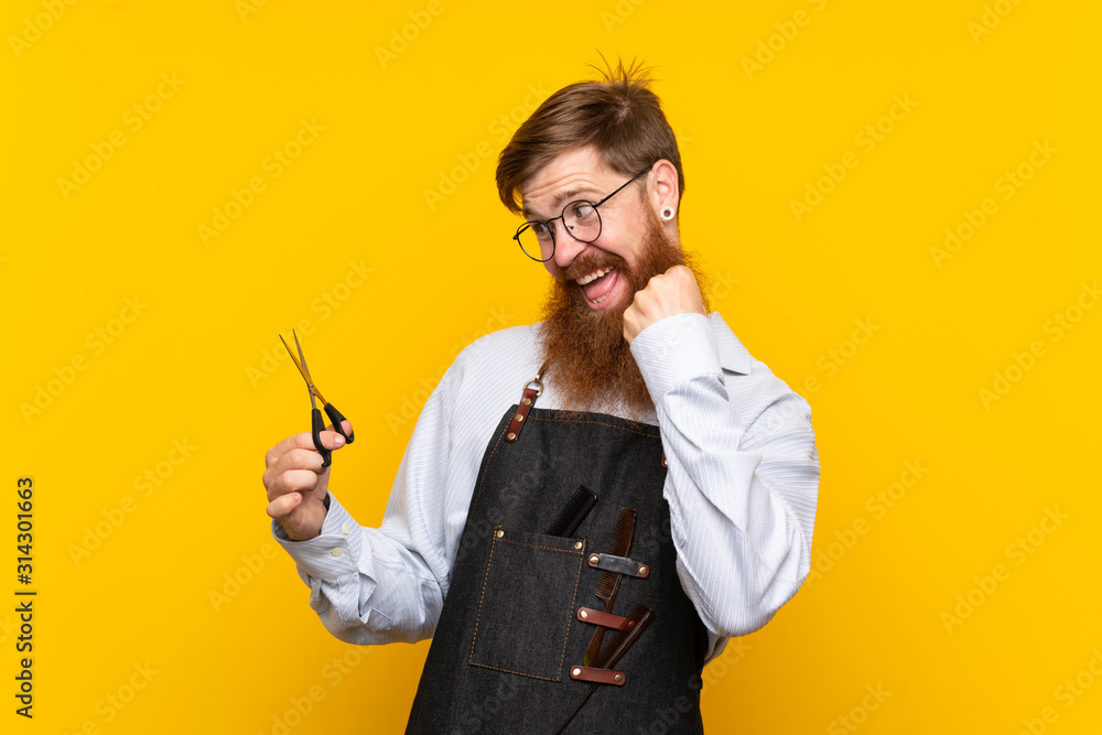 Barber with long beard in an apron over isolated yellow background celebrating a victory Barber with long beard in an apron over isolated yellow background celebrating a victory