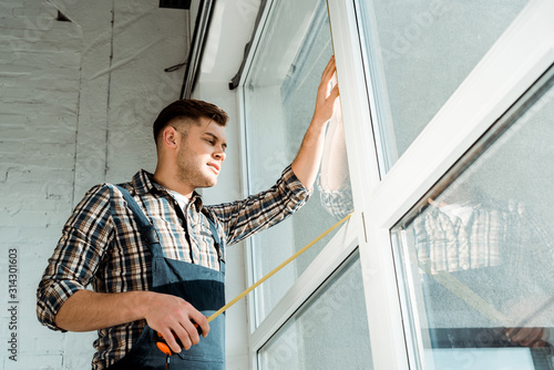 low angle view of installer standing near windows and holding measuring tape photo