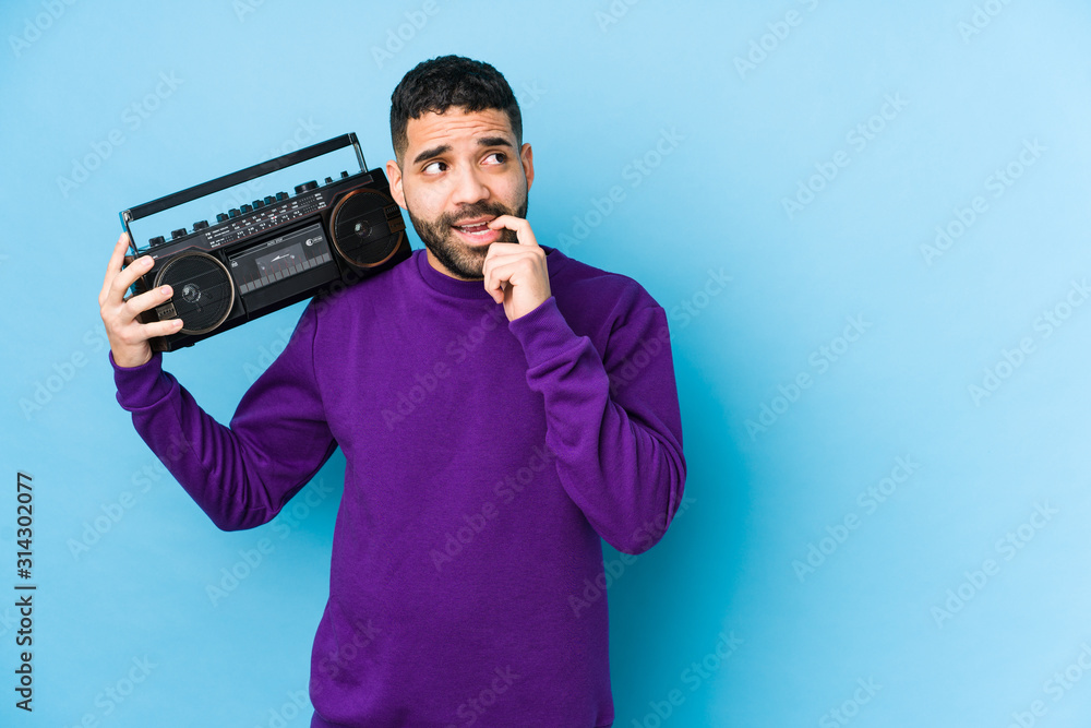 Young arabian man holding a radio cassette isolated Young arabian man listening music relaxed thinking about something looking at a copy space. Young arabian man holding a radio cassette isolated Young arabian man listening music relaxed thinking about something looking at a copy space.
