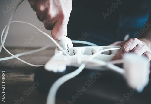 close-up of hand plugging power cable into power strip outlet photo