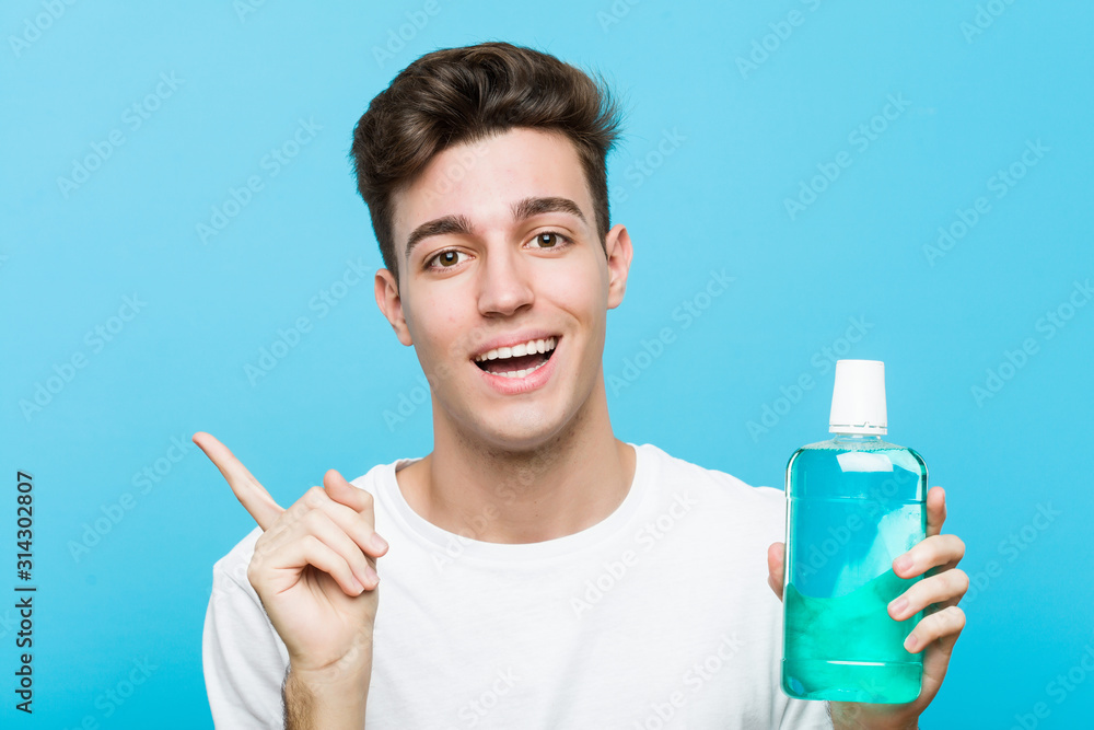 Young caucasian man holding a mouthwash smiling cheerfully pointing with forefinger away. Young caucasian man holding a mouthwash smiling cheerfully pointing with forefinger away.