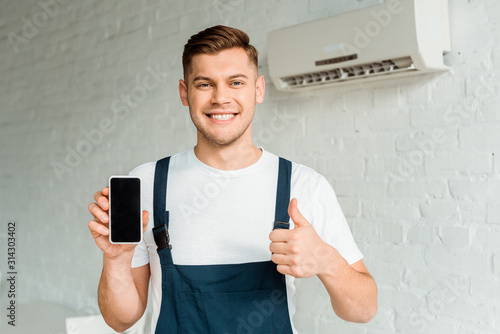 Tableau sur toile cheerful installer showing thumb up while holding smartphone with blank screen