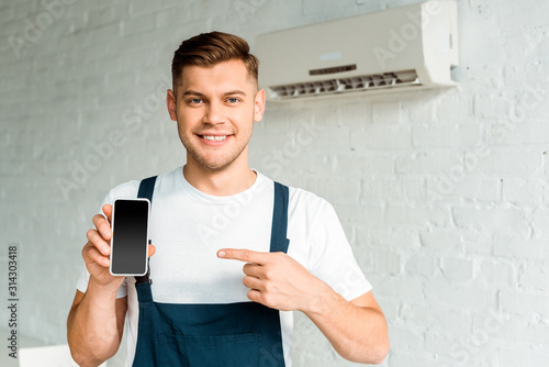 cheerful installer pointing with finger at smartphone with blank screen photo