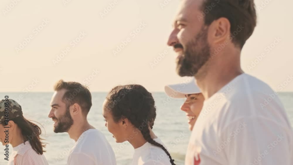Side view of young eco volunteers people are going at the seaside before start to cleaning the beach from garbage early in the morning Side view of young eco volunteers people are going at the seaside before start to cleaning the beach from garbage early in the morning