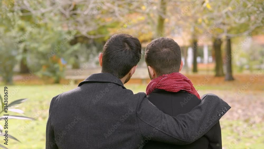young gay man embracing his boyfriend on a bench at park young gay man embracing his boyfriend on a bench at park