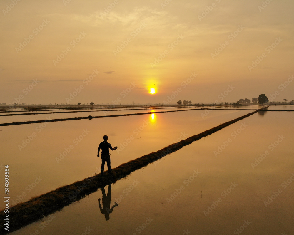 Silhouette of man walking toward sunset with reflection on the water.