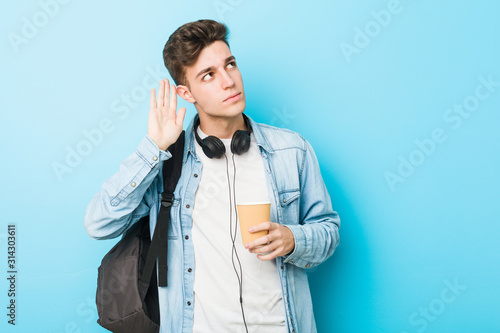 Young caucasian student man holding a take away coffee trying to listening a gossip.