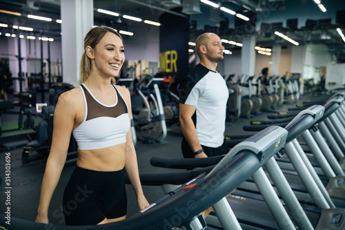 young beautiful girl and guy doing exercises in the gym, jogging on the track indoors, fitness and crossfit