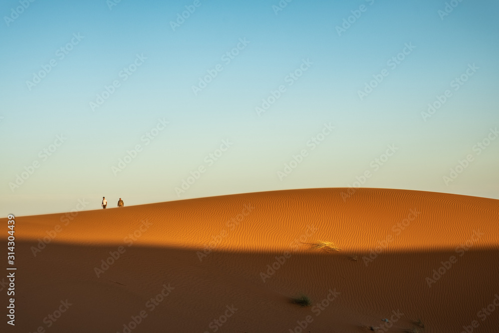 Dos personas caminando sobre dunas en el desierto al atardecer. Erg Chebbi, Marruecos.