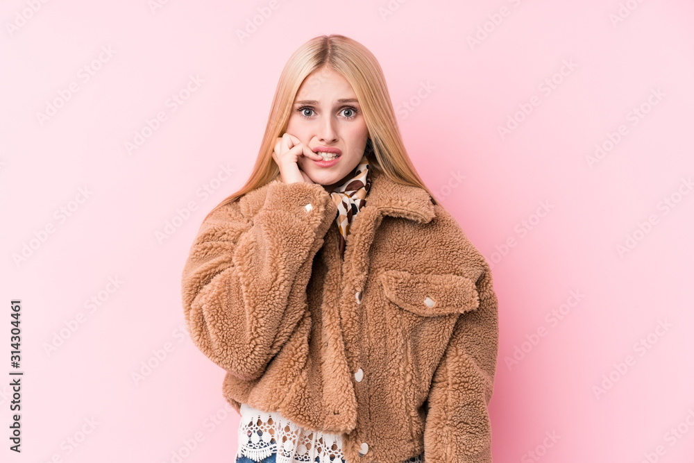 Young blonde woman wearing a coat against a pink background biting fingernails, nervous and very anxious. Young blonde woman wearing a coat against a pink background biting fingernails, nervous and very anxious.