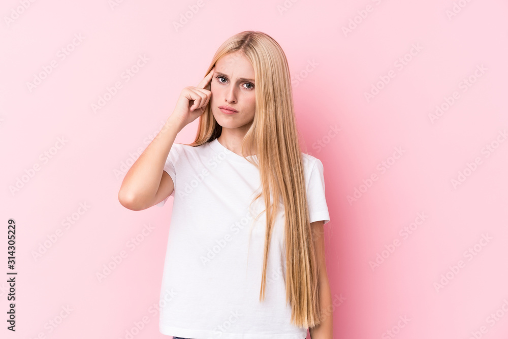 Young blonde woman on pink background pointing temple with finger, thinking, focused on a task. Young blonde woman on pink background pointing temple with finger, thinking, focused on a task.