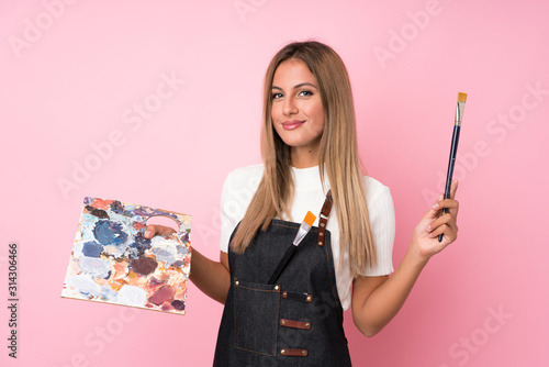 Young blonde woman over isolated pink background holding a palette