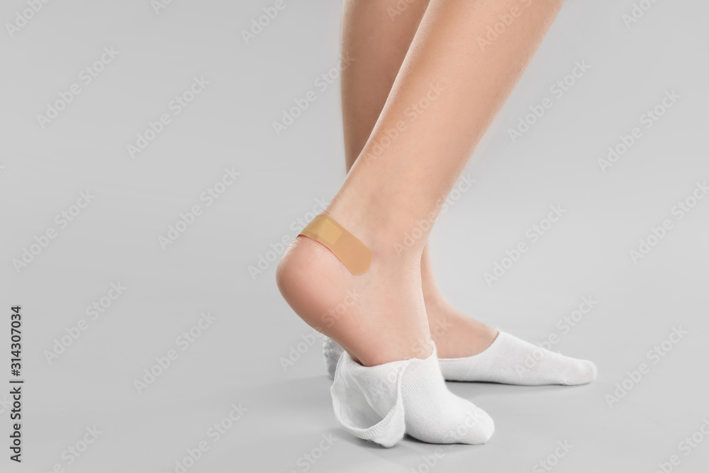 Girl showing foot with sticking plaster on light grey background, closeup