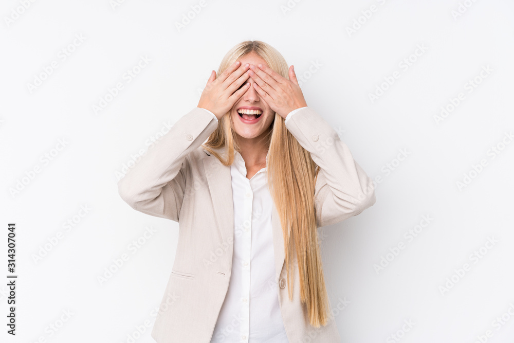 Young business blonde woman on white background covers eyes with hands, smiles broadly waiting for a surprise. Young business blonde woman on white background covers eyes with hands, smiles broadly waiting for a surprise.