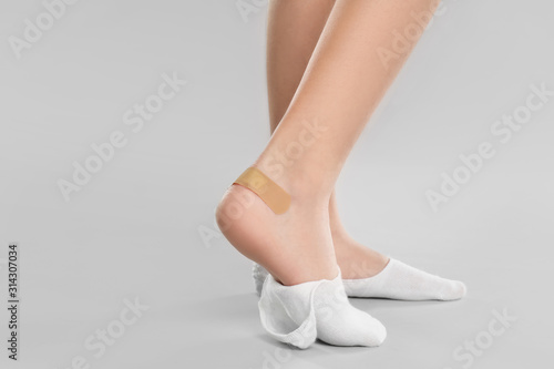 Girl showing foot with sticking plaster on light grey background, closeup