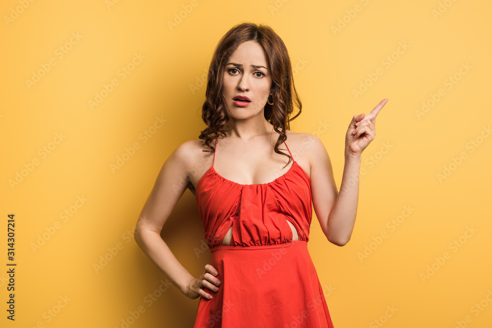 displeased girl pointing with finger while standing with hand on hip on yellow background displeased girl pointing with finger while standing with hand on hip on yellow background