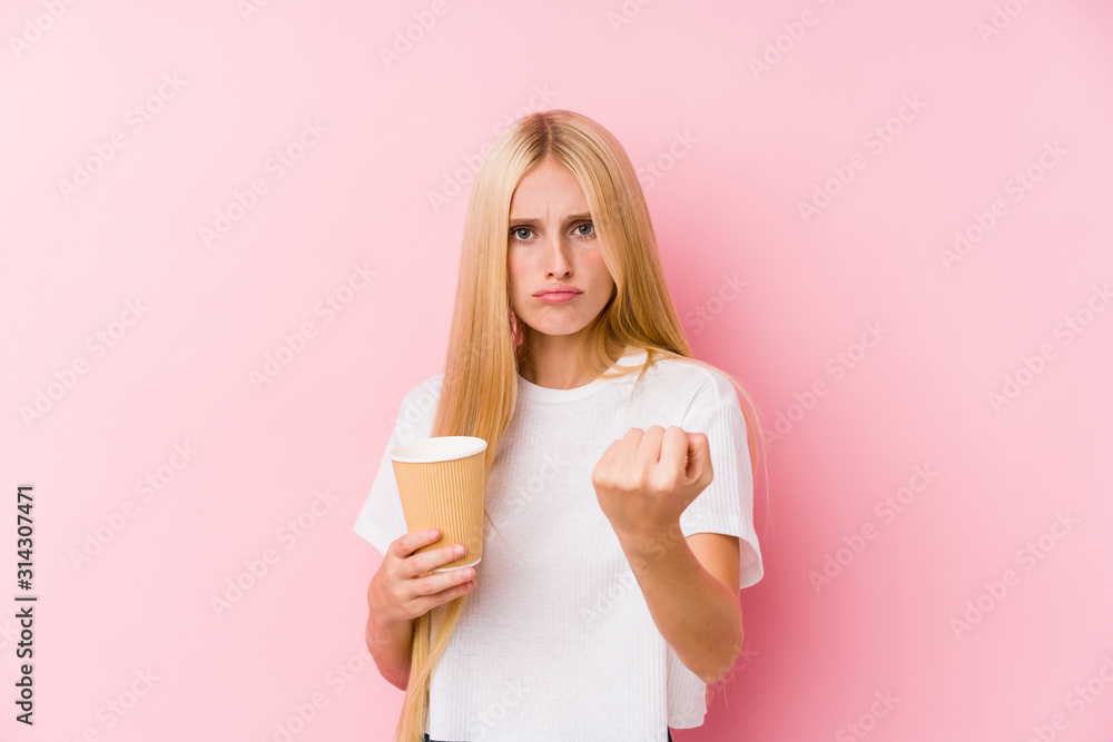 Young blonde girl holding a takeaway coffee showing fist to camera, aggressive facial expression. Young blonde girl holding a takeaway coffee showing fist to camera, aggressive facial expression.