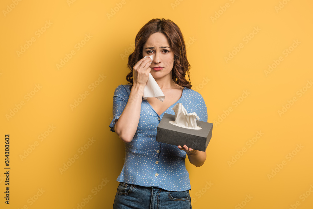 upset girl covering tears with paper napkin on yellow background upset girl covering tears with paper napkin on yellow background