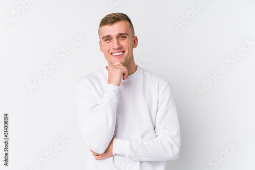 Young caucasian man on white background smiling happy and confident, touching chin with hand.
