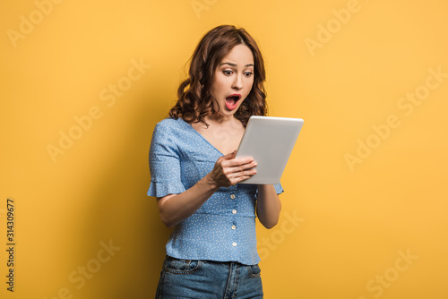 shocked woman using digital tablet on yellow background