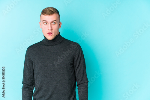 Young caucasian man on a blue background being shocked because of something she has seen.