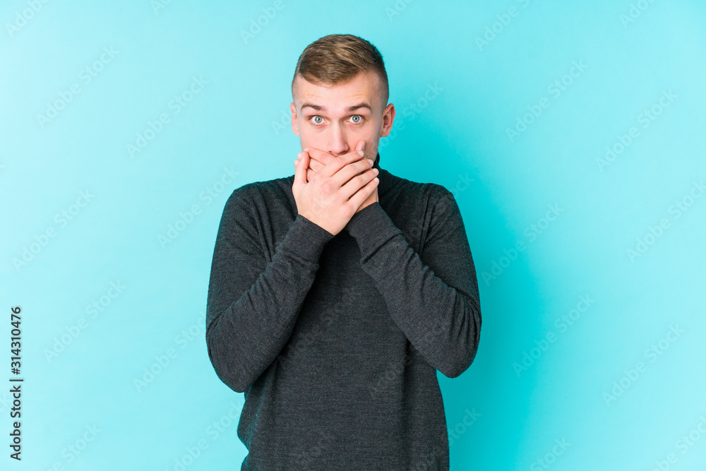 Young caucasian man on a blue background shocked covering mouth with hands. Young caucasian man on a blue background shocked covering mouth with hands.