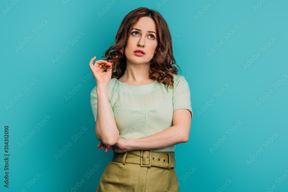 dreamy woman looking up and touching hair while standing on blue background dreamy woman looking up and touching hair while standing on blue background