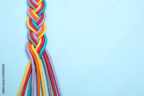 Top view of braided colorful ropes on light blue background, space for text. Unity concept