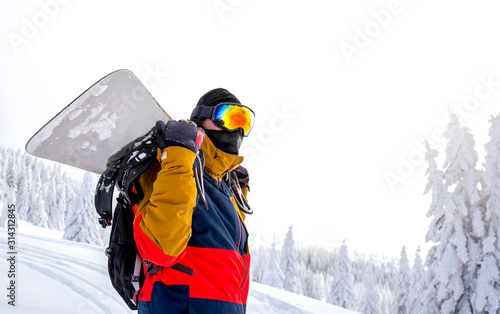 Active  snowboarder having break at the top of the hill with beautiful winter landscape in the background