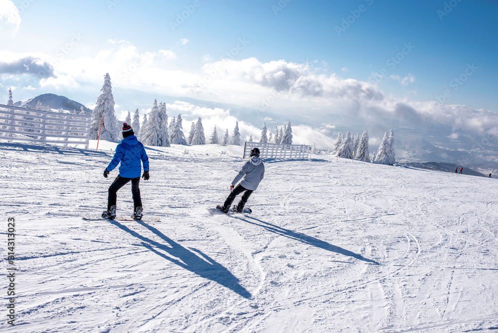 Active male snowboarders enjoy riding snowboard down the slope with beautiful winter landscape in the background
