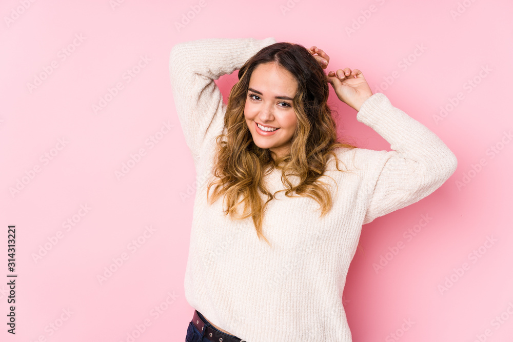Young curvy woman posing in a pink background isolated stretching arms, relaxed position. - obrazy, fototapety, plakaty 
