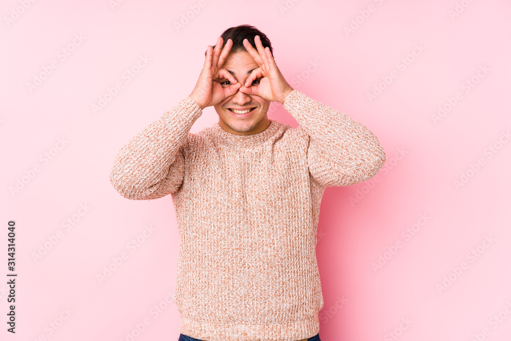 Young curvy man posing in a pink background isolated showing okay sign over eyes