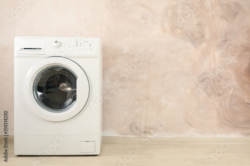 Modern washing machine against brown wall, space for text