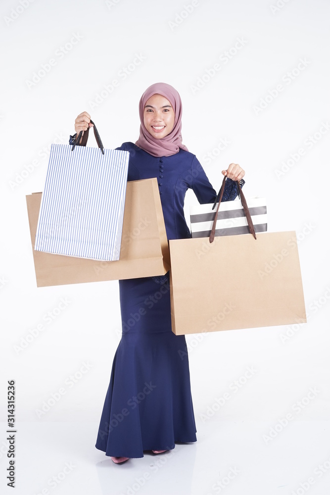 A beautiful and excited Muslim female model in a Asian traditional dress modern kebaya carrying shopping bags isolated on white background. Eidul fitri fashion and festive preparation shopping concept A beautiful and excited Muslim female model in a Asian traditional dress modern kebaya carrying shopping bags isolated on white background. Eidul fitri fashion and festive preparation shopping concept