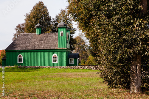 Green wooden building (mosque) with white window frames, stone fence in front of it. Broadleaved tree in foreground. Kruszyniany, Poland, Europe. photo