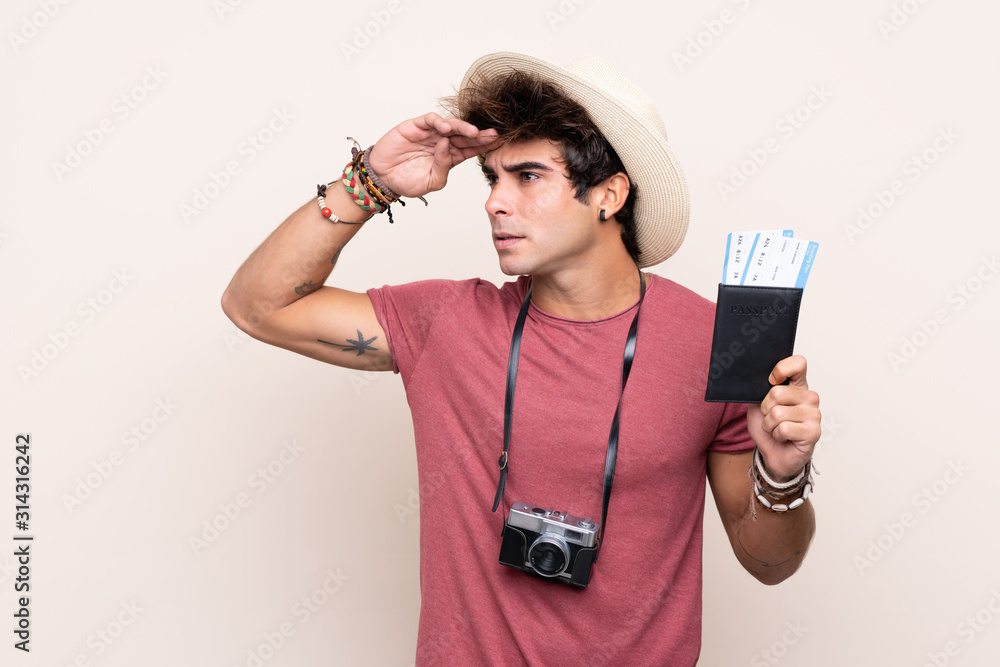 Young caucasian man over isolated background in vacation with passport and plane tickets while looking something in the distance Young caucasian man over isolated background in vacation with passport and plane tickets while looking something in the distance