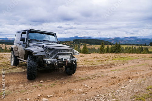 Black jeep parked by the road with picturesque mountain, forests and clouds panorama on the background.