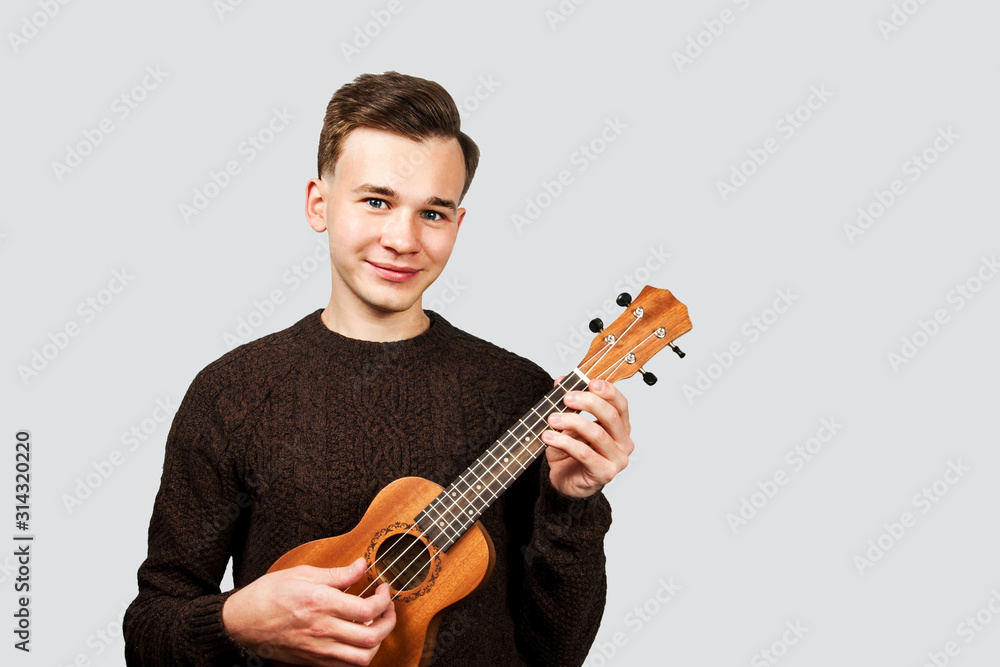 portrait White young guy in sweater play on ukulele in his hands, isolated
